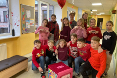 4.b klase ar klases audzinātāju ģērbušies sarkanos toņos fotogrāfējas skolas gaitenī 